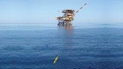 Gavia AUV by Teledyne in ocean with oil rig in distance